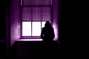 Donna vittima di stalking che osserva preoccupata la strada dalla finestra di casa.