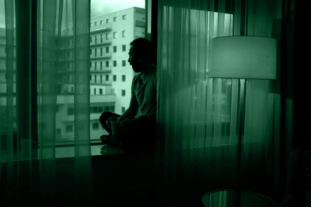 Uomo che guarda fuori dalla finestra al buio, simboleggia l’ansia e l’influenza del true crime sulla percezione del rischio.