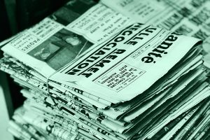 Fascio di vecchi giornali legati con uno spago, appoggiati su un tavolo di legno, simbolo della narrazione del crimine attraverso i media.