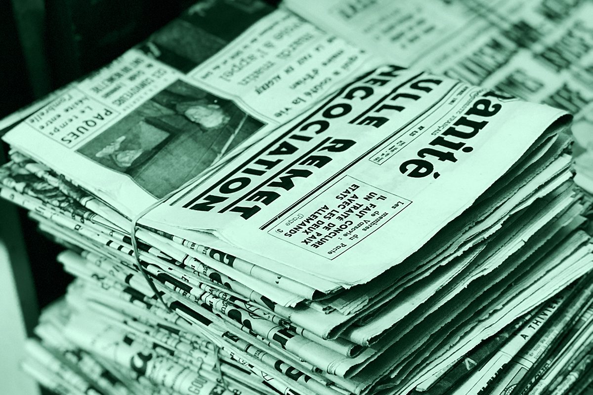 Fascio di vecchi giornali legati con uno spago, appoggiati su un tavolo di legno, simbolo della narrazione del crimine attraverso i media.