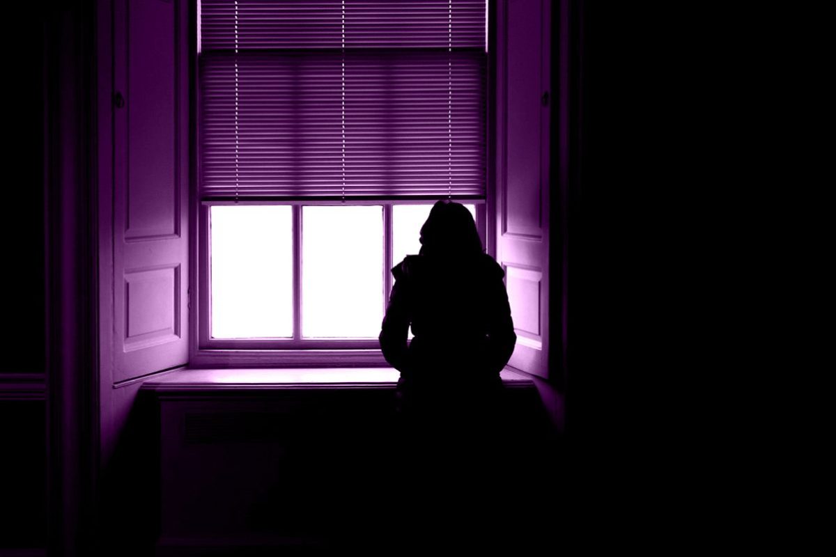 Donna vittima di stalking che osserva preoccupata la strada dalla finestra di casa.