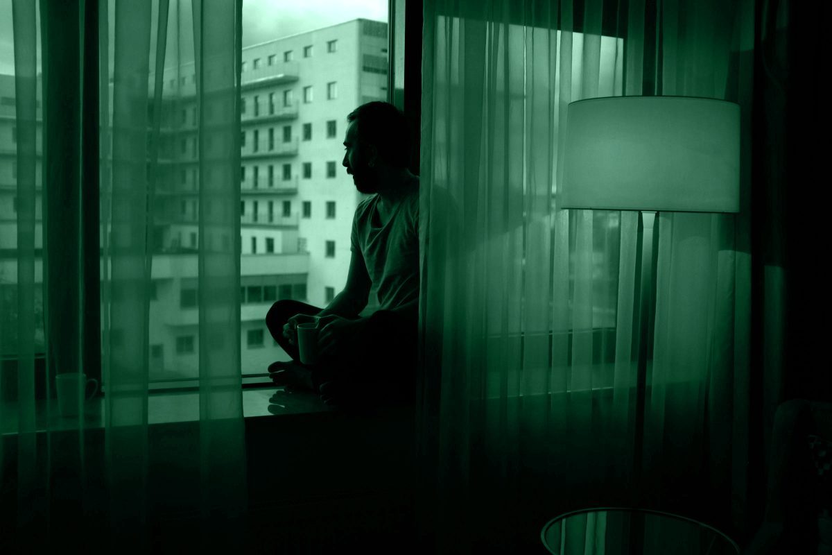 Uomo che guarda fuori dalla finestra al buio, simboleggia l’ansia e l’influenza del true crime sulla percezione del rischio.
